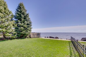 Guests can enjoy a serene lawn surrounded by a natural backdrop of an evergreen tree and a body of water.