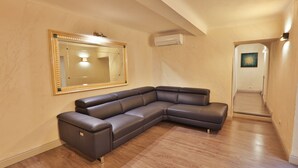 A modern living room with a sectional sofa, hardwood flooring, a large mirror, and an air conditioning unit. - Grottini Luxury Suites - Pantheon (Rome)