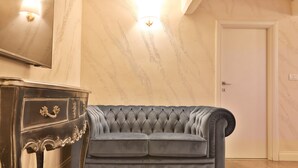 A room with a tufted grey sofa, a dark wooden dresser with ornate handles, and a light switch on the wall. - Grottini Luxury Suites - Pantheon (Rome)