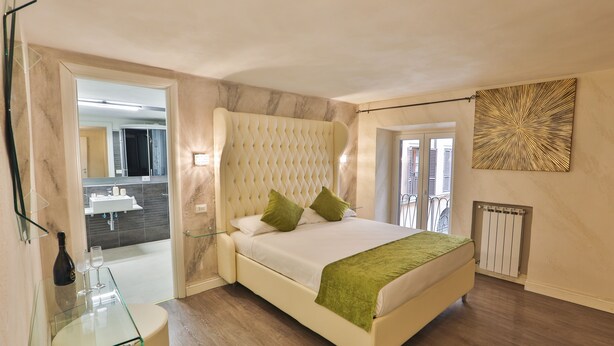 A bedroom with a bed, a glass table, a mirror, a radiator, and a view of the bathroom. - Grottini Luxury Suites - Pantheon (Rome)