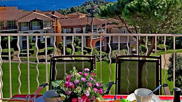 A balcony with a table set for two, overlooking a coastal view with houses and a clear sky. - Apartment Cap Esterel sea view with reversible air conditioning (Saint-Raphaël)