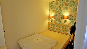 A single bed with a wooden headboard, two wall-mounted lamps, and a tropical leaf-patterned wallpaper. - Apartment Cap Esterel sea view with reversible air conditioning (Saint-Raphaël)