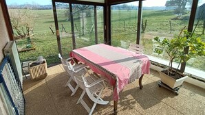 A room with a table and chairs, large windows, and a view of a green field.
