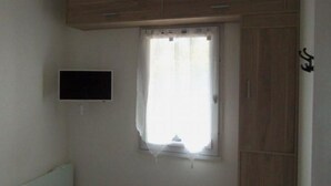A room with a wooden wardrobe, a small television mounted on the wall, and a window with a curtain. - Maison Tout Confort à Lacanau Océan (Lacanau)