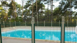 A rectangular swimming pool surrounded by a green metal fence, with trees in the background. - Maison Tout Confort à Lacanau Océan (Lacanau)