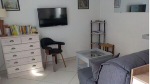 A living room with a sofa, a chair, a TV, a bookshelf, and a small table. - Maison Tout Confort à Lacanau Océan (Lacanau)