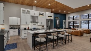 Una cocina moderna con armarios blancos, una isla central con taburetes de bar, un refrigerador de acero inoxidable y un amplio ventanal con vistas a un paisaje nevado.