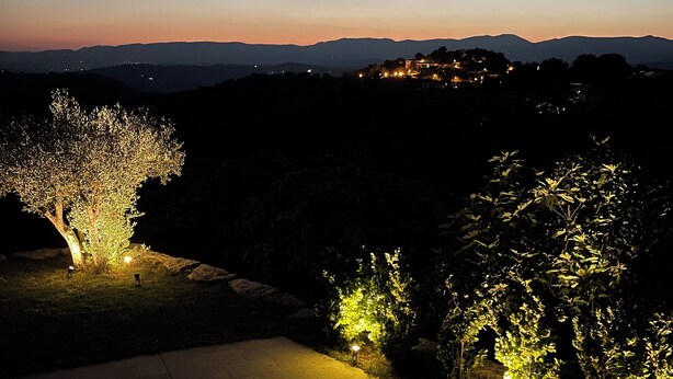 A nighttime view of a landscaped area with illuminated trees and a distant mountain range. - Villa Provençale Tout Confort Avec vue (Tanneron)