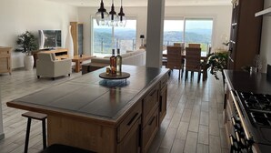 A modern kitchen with a large island, dining area with wicker chairs, and a view of the mountains through large windows. - Villa Provençale Tout Confort Avec vue (Tanneron)