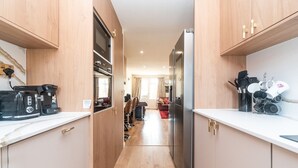 A narrow kitchen with wooden cabinets, a stainless steel refrigerator, and a coffee maker on the counter. - Spacious Cosy Home Close To London Abbey Wood - Pass the Keys (London)