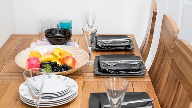 A wooden dining table set with plates, cutlery, glasses, and a fruit bowl. - Spacious Cosy Home Close To London Abbey Wood - Pass the Keys (London)