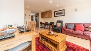 A modern living room with a wooden dining table set for four, a red shag rug, a leather sofa with cushions, and a framed picture on the wall. - Spacious Cosy Home Close To London Abbey Wood - Pass the Keys (London)
