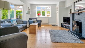 Ein geräumiges Wohnzimmer mit Kamin, einer Sofagarnitur, einem Couchtisch und einem großen Fenster mit Blick auf Grünflächen.