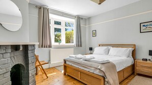Ein Schlafzimmer mit einem Holzbett, einem Kamin, einem fenster mit Vorhängen, einer Heizung und einem kleinen Tisch mit einer Lampe.