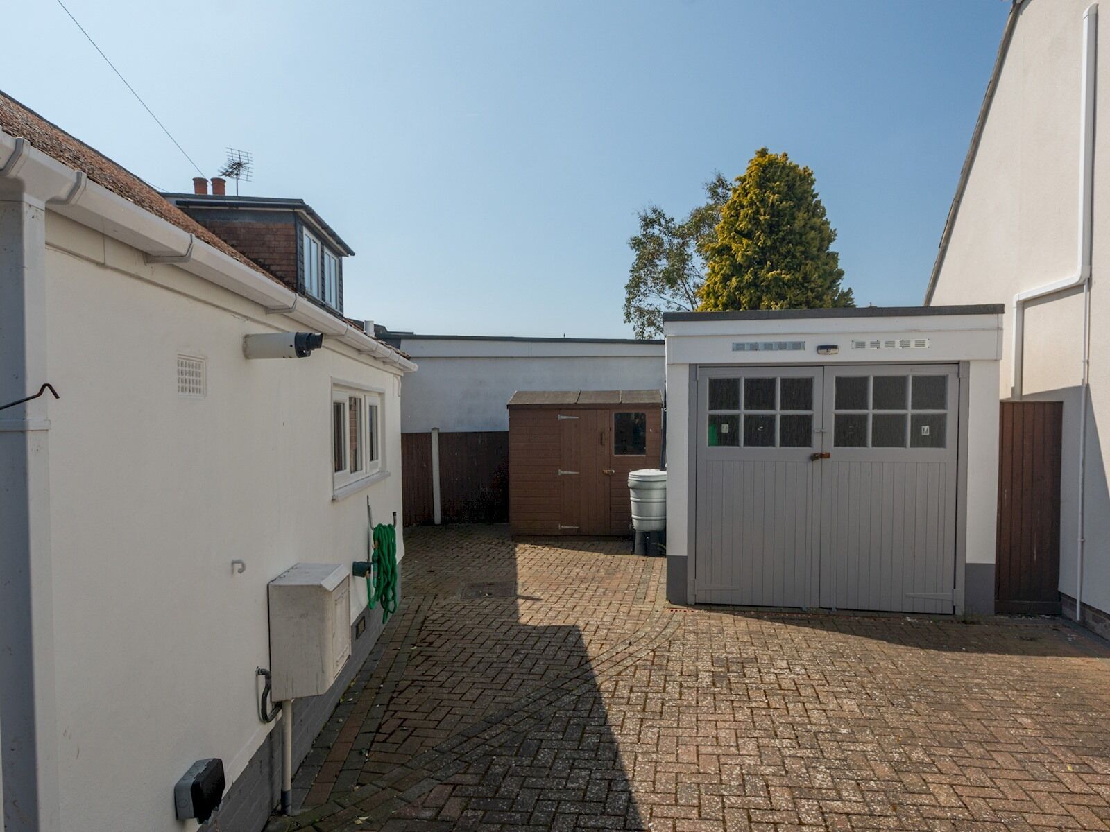 Un vialetto di mattoni che conduce a un edificio bianco con un garage e un capanno di legno.