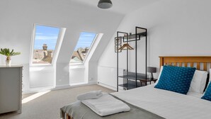 Ein Schlafzimmer mit Bett, Nachttisch, Hängekorbschaukel und Fenster mit Blick auf Gebäude.