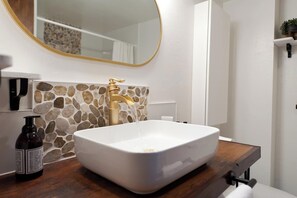 A bathroom with a white sink, gold faucet, and a stone backsplash. There is a bottle of hand soap on the counter and a mirror above the sink. - Iron Horse Hideaway | AC, Pool, Hot Tub, Golf & Ski (Durango)