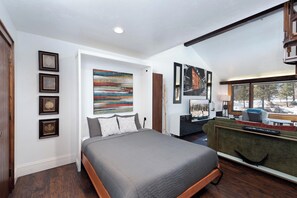 A modern bedroom with a large bed, a desk, and a view of a snowy landscape through a window. - Iron Horse Hideaway | AC, Pool, Hot Tub, Golf & Ski (Durango)