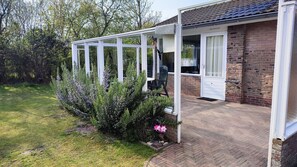 Een huis met een overdekte veranda, een bakstenen gevel en een tuin met struiken en bloemen.