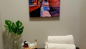 Una consola de madera con una obra enmarcada, un florero con una planta y una cesta con artículos de aseo.