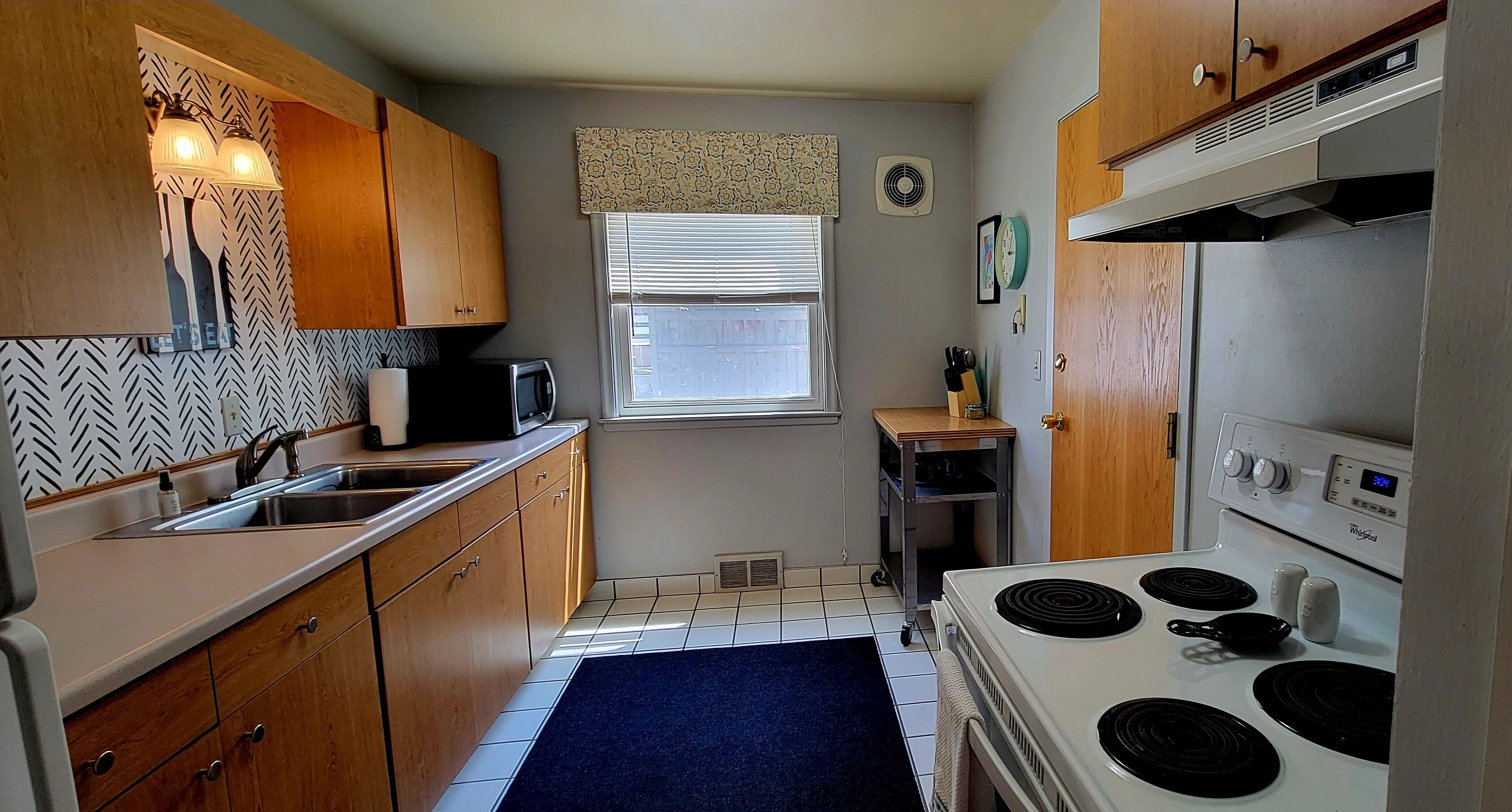 A compact kitchen with wooden cabinets, a microwave, a stove, and a small window.