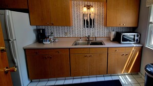 Una cocina compacta con armarios de madera, un refrigerador blanco, una cafetera, un microondas y un lavamanos.