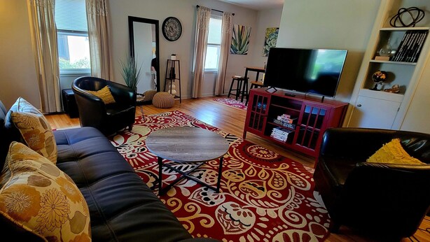 Una sala de estar con un sofá, un televisor, un mueble rojo y una alfombra estampada.