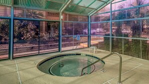 En inomhuspool med en glasvägg runt om, omgiven av ett staket av metall, och en liten pall placerad nära poolen.