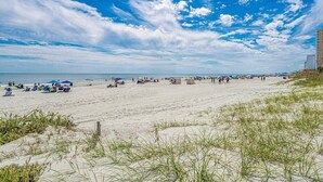 En strand med folk, parasoller och en byggnad i bakgrunden.