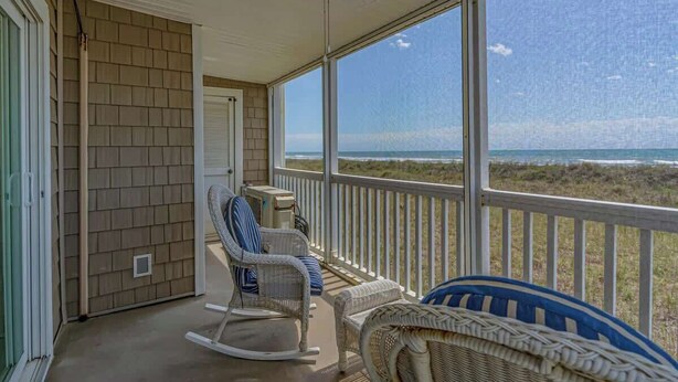 Une véranda couverte, meublée de meubles en osier, dotée d’un ventilateur de plafond et offrant une vue sur la plage.