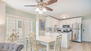 Une cuisine moderne avec des meubles blancs, des appareils en acier inoxydable et un coin repas comprenant une table et des chaises blanches.