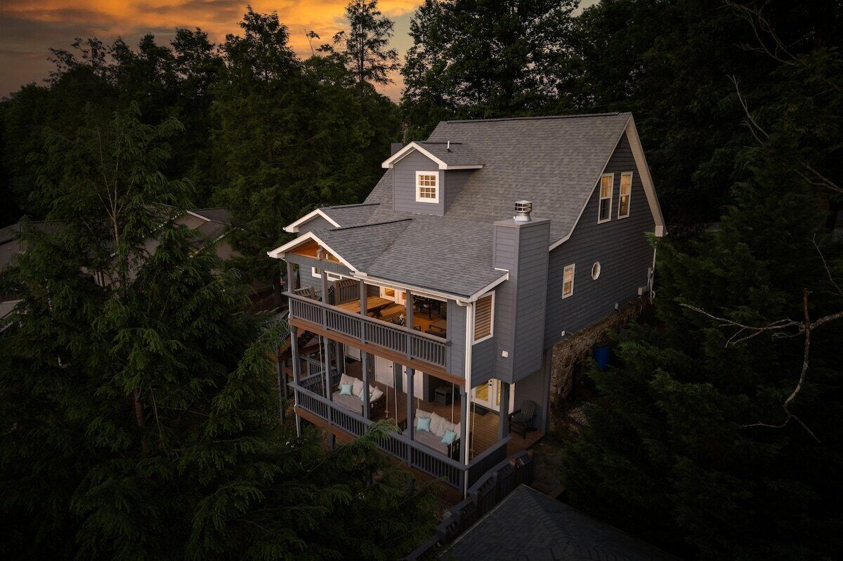 A two-story house with a balcony, surrounded by dense trees.