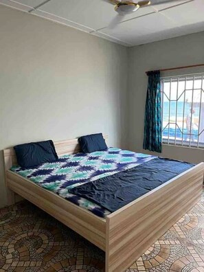 Un dormitorio con cama, dos almohadas, una ventana con cortinas y suelo estampado.