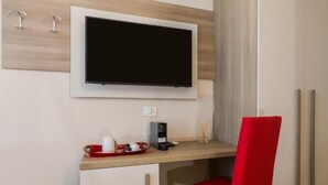 A hotel room with a flat-screen TV mounted on the wall, a desk with a tray of breakfast items, a red chair, and a bed with a wooden headboard. - VRooms All'Angolo Del Duomo (Florence)