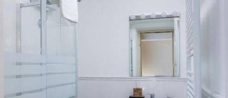 Un baño moderno con cabina de ducha de vidrio, lavamanos pedestal y espejo sobre él.