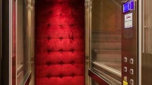 An elevator with a red velvet wall, a digital display, and a small bench. - VRooms All'Angolo Del Duomo (Florence)