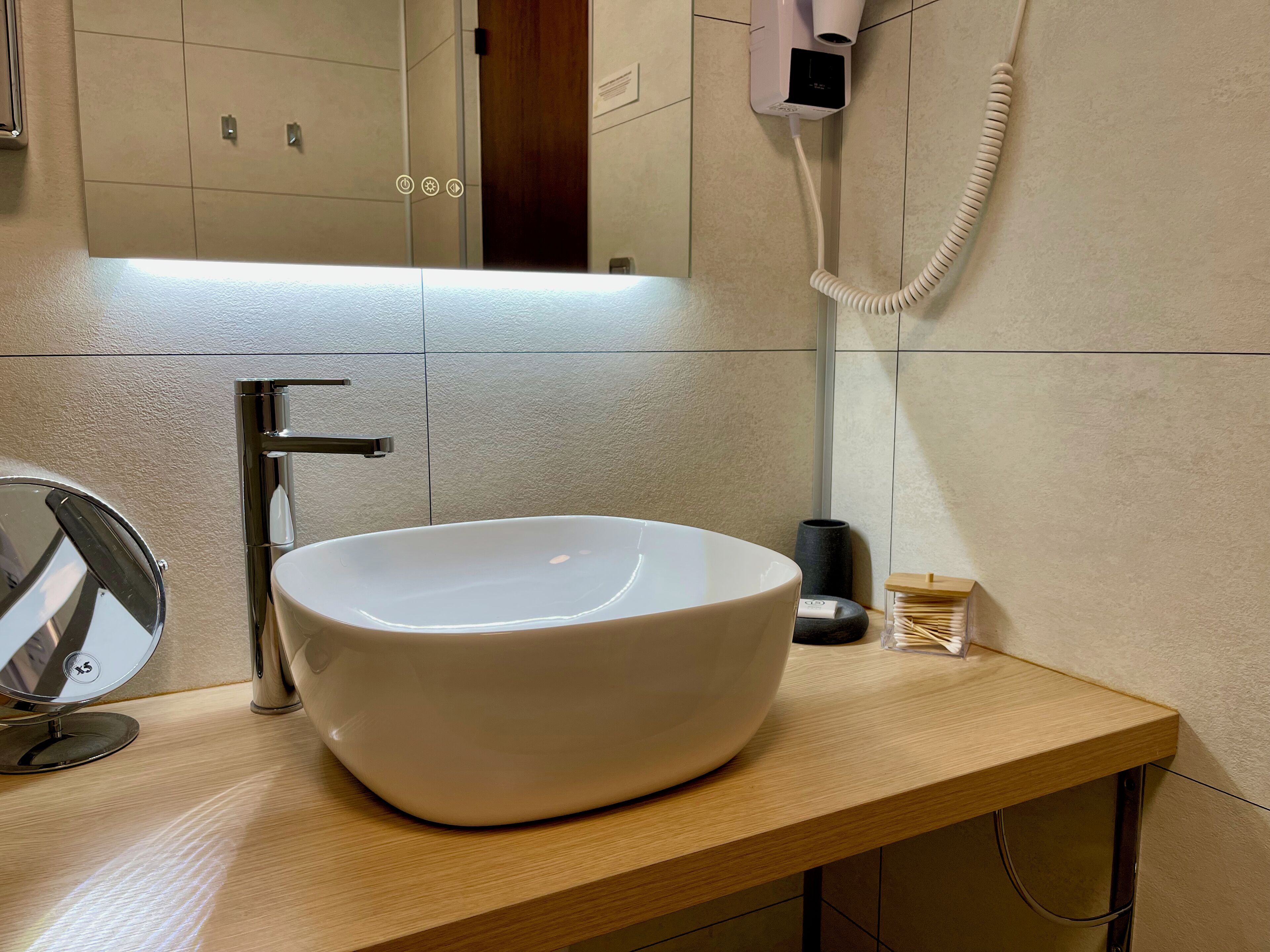 A modern bathroom with a large white sink, a chrome faucet, and a hairdryer mounted on the wall.