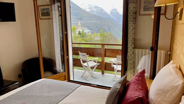 Une chambre d’hôtel avec un lit, un bureau, une chaise et un balcon offrant une vue sur les montagnes.