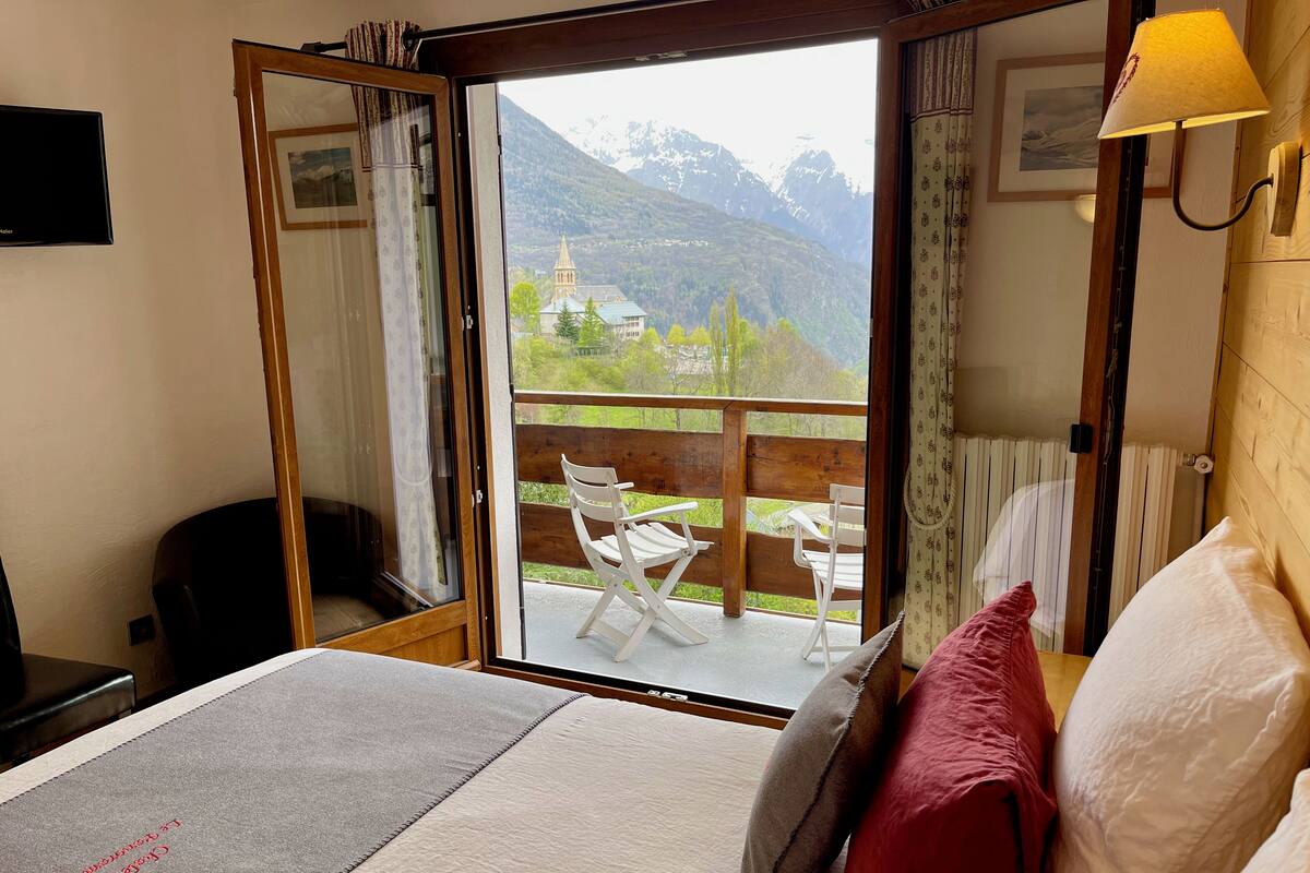 Ein Hotelzimmer mit Bett, Schreibtisch, Stuhl und einem Balkon mit Bergblick.