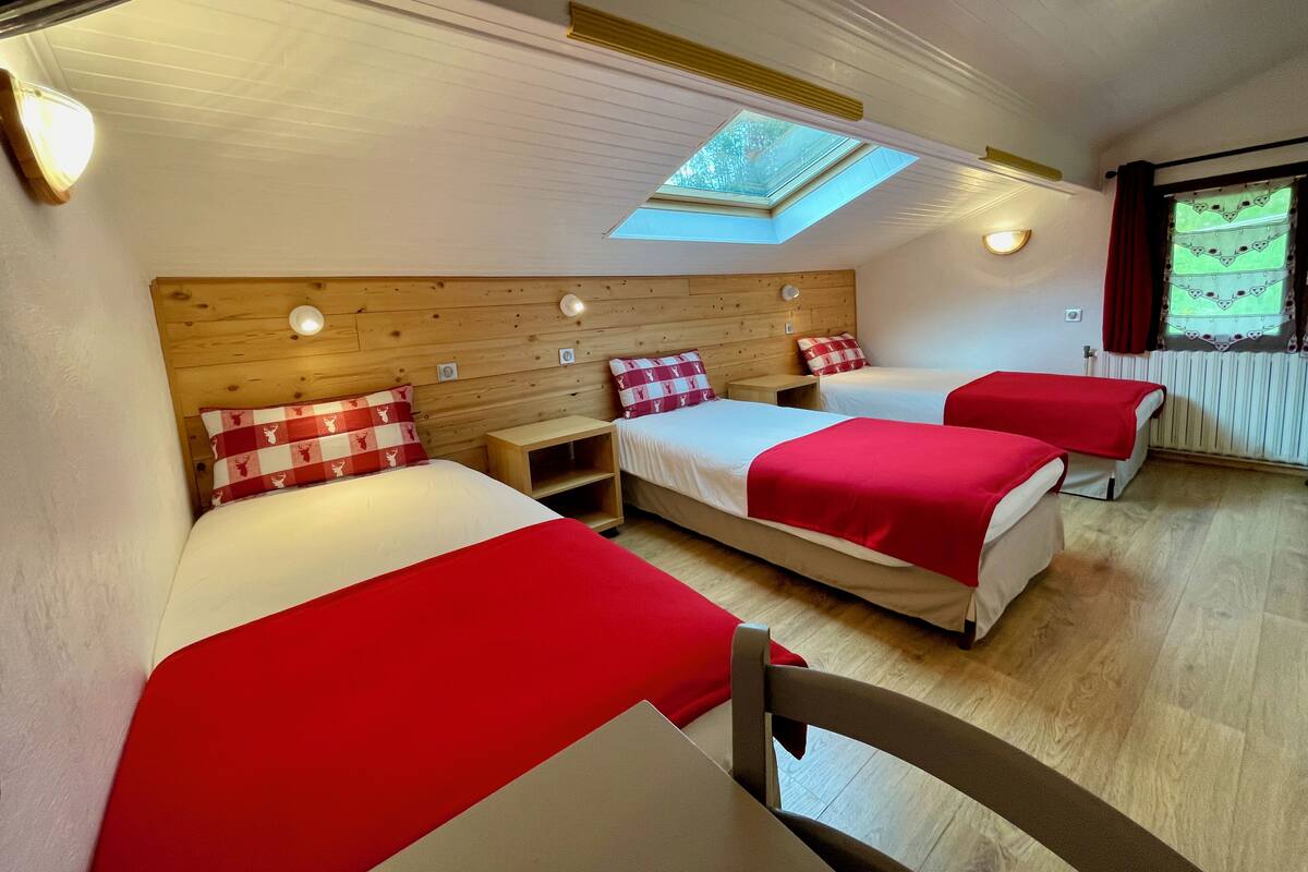 Ein Zimmer mit drei Betten, Holz-Kopfteilen, einem Oberlicht und einem Fenster mit Vorhängen.