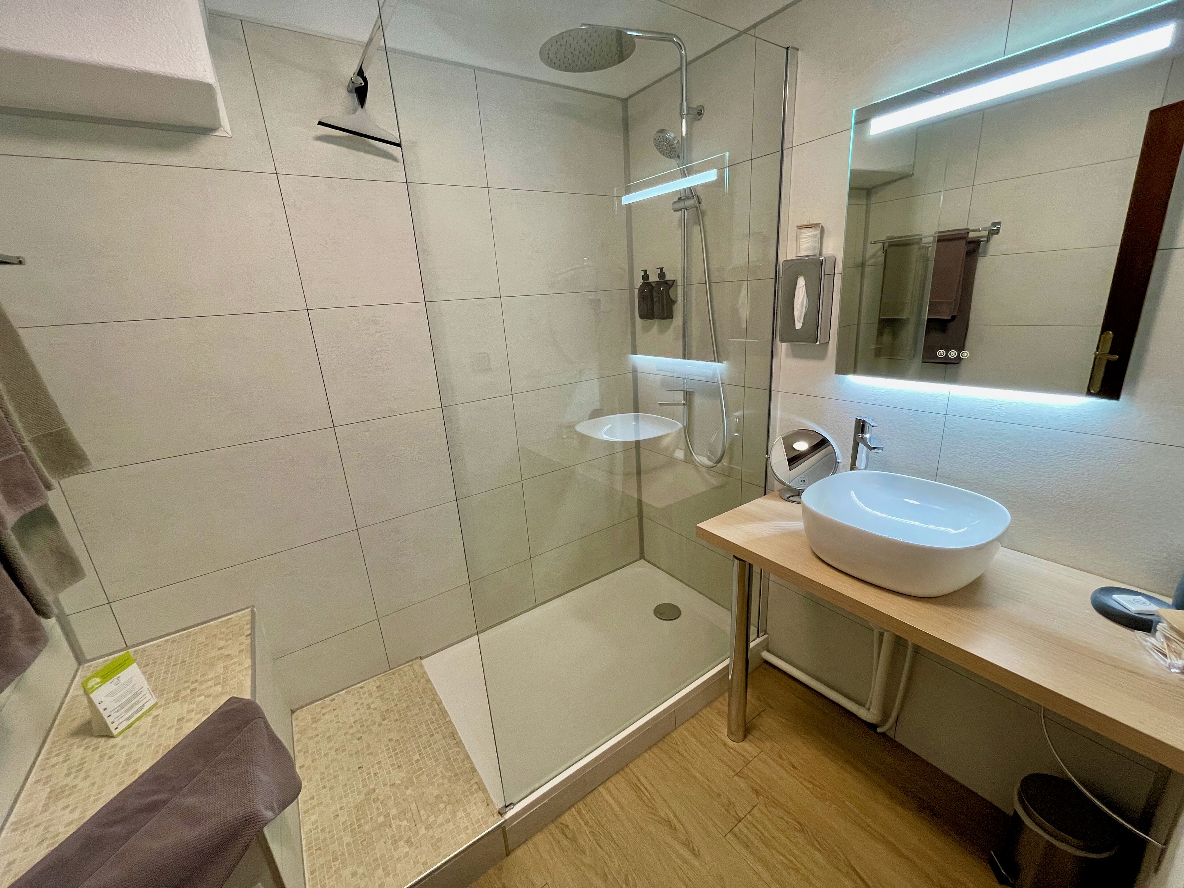 A modern bathroom with a glass-enclosed shower, a wooden vanity with a white sink, and a mirror above the sink.