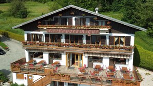 Un bâtiment à deux étages doté d’un balcon et d’un espace extérieur aménagé pour s’asseoir, portant l’inscription « Le Panoramique ».
