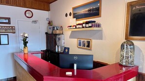 Un comptoir d’accueil avec un plateau rouge, un ordinateur et une horloge au mur.