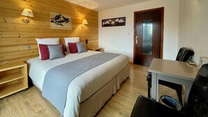 Une chambre avec un mur en bois, un lit avec des oreillers, une table de chevet, un bureau avec une chaise et une porte.