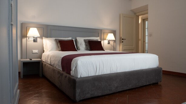 Una cama bien hecha con cabecera gris, dos lámparas de noche y una mesita de noche.