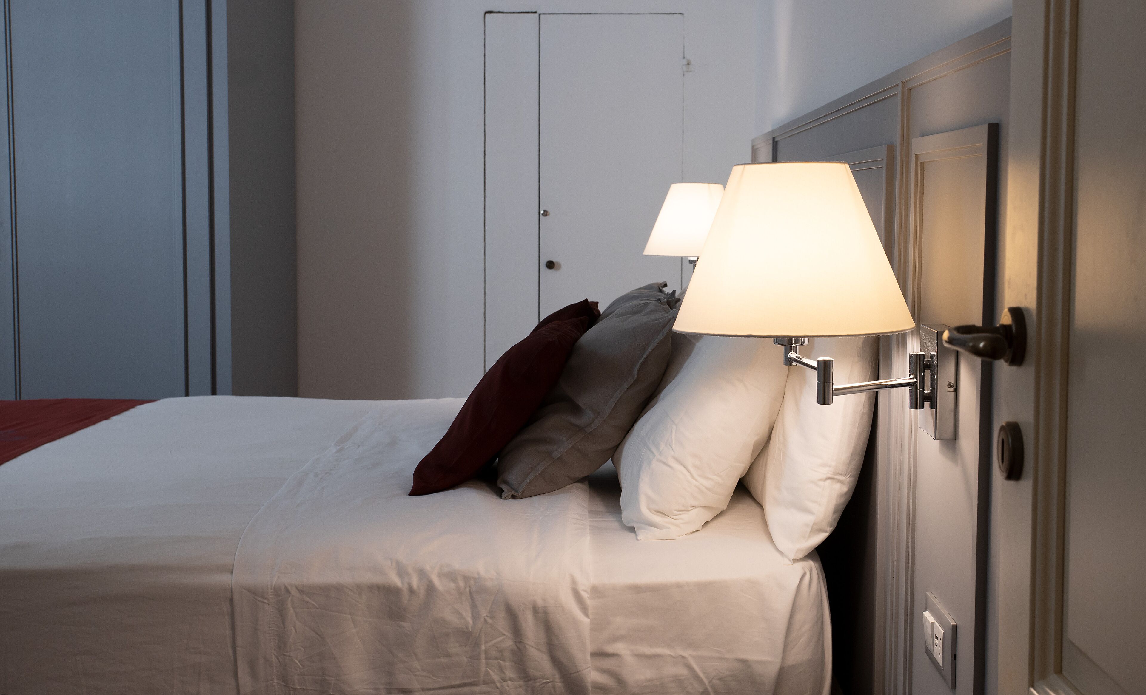 Een net opgemaakt bed met kussens, een bedlampje en een deur met slot.