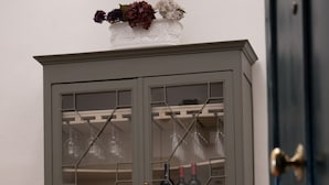 Un mueble gris con puertas de cristal, dos cajones y un jarrón con flores encima.