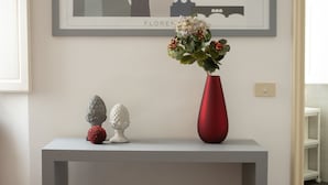 Una habitación moderna con una consola gris, un florero rojo con flores y un otomano gris.