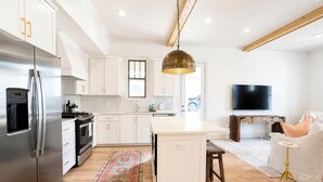 A modern kitchen with white cabinets, a stainless steel refrigerator, a central island, and a large pendant light. - The Mae, 3BR Luxe Home by Velvet Ditch Villas (Oxford)