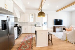 Une cuisine moderne avec des meubles blancs, un réfrigérateur en acier inoxydable, un ßlot central et un grand luminaire suspendu.